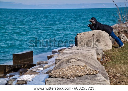 Woman photographer shooting the waves as they splash up from the south shore of Chicago's Lake Michigan on a chilly winter day.