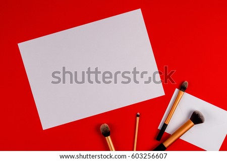 Make up brushes with white blank paper on red background. Top view. Flat lay. Copy space for text