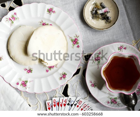 Old fashioned ladies bridge party table setting including vintage tea set, cookies, cigarette, and hand of cards on white linen tablecloth background