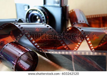 Various uncoiled film (negatives) with pictures lies next to an old camera with a lens