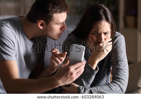 Boyfriend asking for an explanation to his cheater sad girlfriend sitting on a couch in the living room in a house interior with a dark background Royalty-Free Stock Photo #603284063
