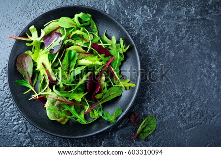 Mix fresh leaves of arugula, lettuce, spinach, beets for salad on a dark stone background. Selective focus. Royalty-Free Stock Photo #603310094