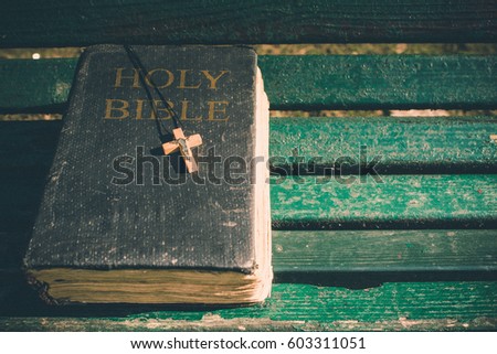 Vintage old holy bible book, grunge textured cover with wooden christian cross. Retro styled image on wood background