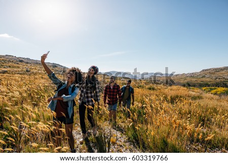 Group of friends taking photograph on country walk. Young men and women hiking in countryside and taking selfie with smart phone.