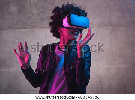 Cheerful girl with hands up wearing the virtual reality goggles. Royalty-Free Stock Photo #603345986