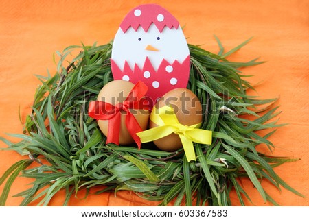 easter decoration: yellow eggs and hand made hatched chicken in eggshell in green grass twigs nest on orange background with copy space