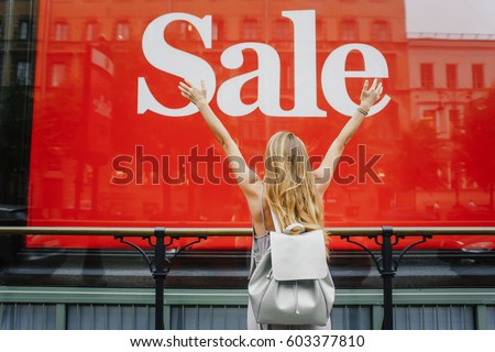 amazing girl Raised hands next to Shop window with sale ad. Red sign on a shop window. Sale in a clothing store