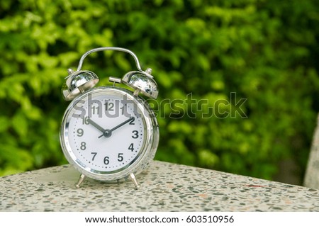 Modern silver alarm clock on gray surface and green soft focus background. 