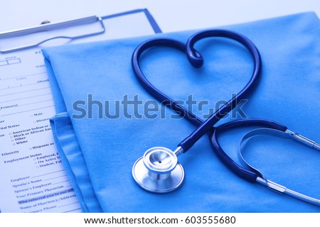 Medical stethoscope twisted in heart shape lying on patient medical history list and blue doctor uniform closeup. Medical help or insurance concept. Cardiology care, health, protection and prevention Royalty-Free Stock Photo #603555680