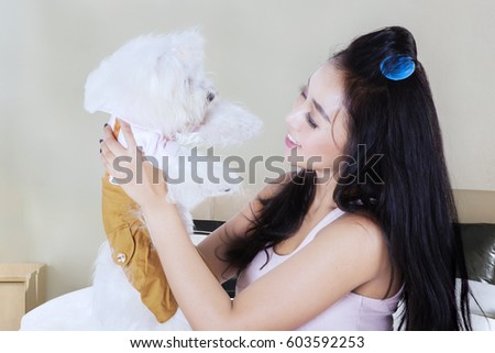 Picture of pretty young woman is holding and smiling with her Maltese dog while sitting on the bedroom