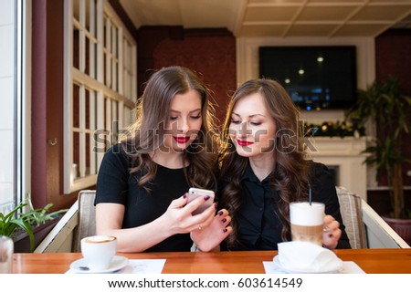 Two beautiful girls drink coffee and look in the phone
