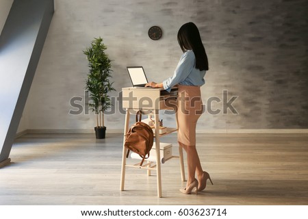 Woman typing on laptop at stand-up workplace Royalty-Free Stock Photo #603623714