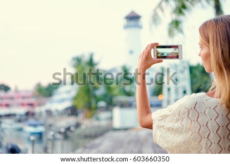 Tourism concept. Young woman  taking photo on smartphone while walking on the seafront.