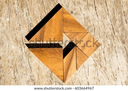 Tangram puzzle as arrow in square shape on wooden background (Concept for business direction and decision)