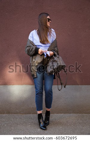 perfect spring fashion outfit. european fashion blogger wearing a trendy crossover striped blouse with a front knot, a bomber jacket, jeans, ankle boots and holding a stylish handbag. 