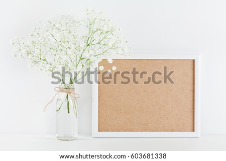Mockup of picture frame decorated flowers in vase on white working desk with clean space for text and design your blogging. 