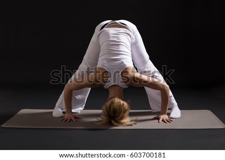 Woman exercising yoga indoors on black background,Yoga -Standing separate leg stretching pose/Padottanasana