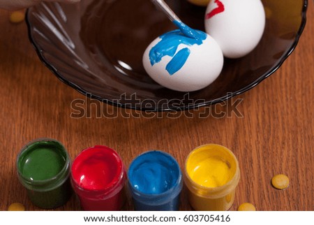 Painting Easter eggs with a brush, paint the egg in a black pot, wooden background,