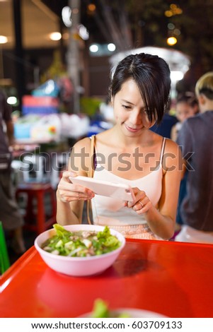 Woman taking photo on her food in outdoor market in Bangkok city