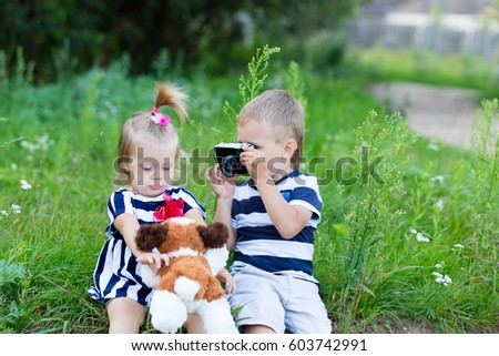 The boy is taking pictures of an old girl in the open air. Little boy and girl are sitting on a stump in the forest while outdoors in summer. Brother and sister are resting in nature