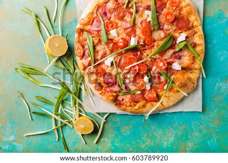 Spring pizza with cherry tomatoes and ham on a turquoise abstract background. 