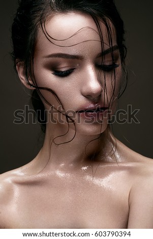 A young girl with shining wet skin and wet hair on her face. Beautiful model with creative bright makeup. Beauty of the face. Photo is made in the studio.