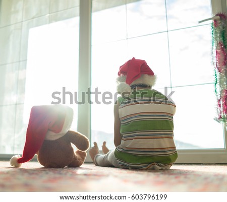 Christmas picture little boy in Santa hat with cute teddy bear sitting in front of window
