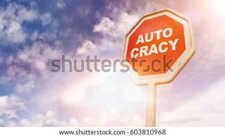 Autocracy, text on red traffic stop sign in front of cloudy blue sky with lens flares