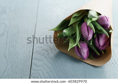 purple tulips in craft paper on blue wood background, with copy space