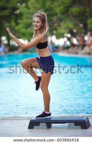 Fitness, training, aerobics, sport concept - Athletic woman trainer at step doing aerobic class with steppers outdoors near pool. Fitness woman with step platform doing work out at tropical resort