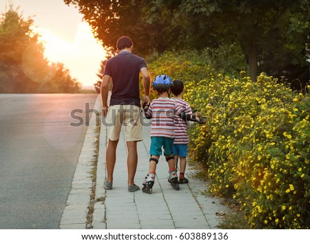 Father with two children on evening walk, on child with in-line skates learning skating. 