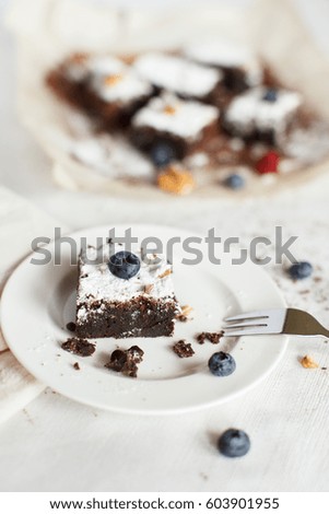 Table setting, chocolate dessert brownie cake with berries on a white plate on a table covered with a linen tablecloth. The second part of the cake on the parchment paper. Vertical image, daylight.