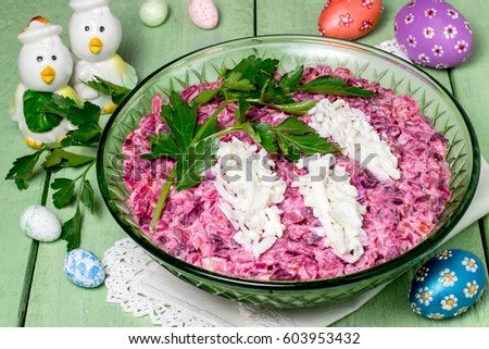 Festive salad with beets, smoked fish and egg on a green wooden table with eggs and chickens. Original decoration in form of flowering twig of bird cherry. Easter treat, Easter recipe. Selective focus