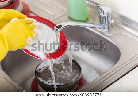Cleaning dishware kitchen sink sponge washing dish. Close up of female hands in yellow protective rubber gloves washing. Royalty-Free Stock Photo #603953771