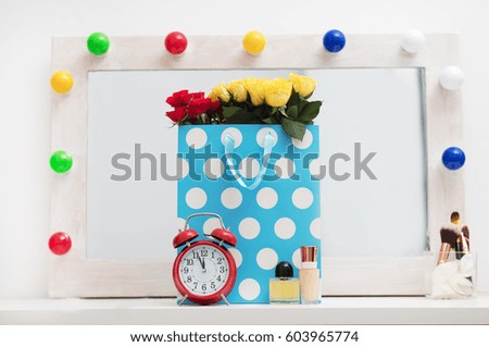 bunch of roses in shopping bag, alarm clock, make up set on the wonderful mirror with lights background
