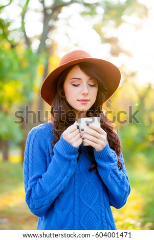 photo of beautiful young woman with cup of coffee standing in the park