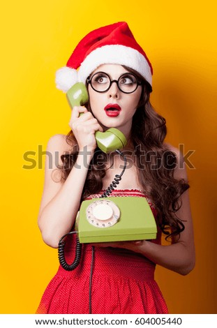 photo of beautiful young woman with retro phone in santa claus hat on the wonderful yellow background