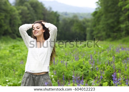 Happy pretty brunette woman in flower field, cute female relaxed on flowers meadow, spring nature, having fun outdoor 