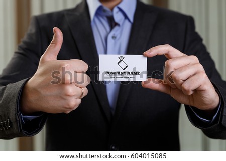 Businessman holding visit card. Man showing blank business card with phone icon. Person in black suit showing thumb up. Mock up design.