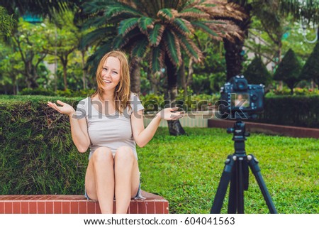 A young female blogger is leading her video blog in front of the camera in the park. Blogger concept.