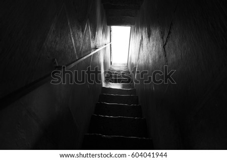 Stairway in black and white. Nice mystical photo of dark steps in stair leading to door in light. Beautiful poetic fine art image. Calm, peaceful and stillness.