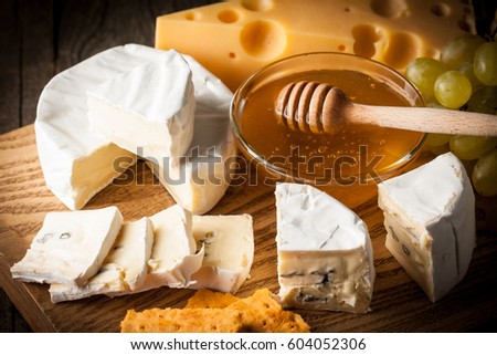 Slate board with various cheese and a glass of red rose wine. Brie. Camembert. Gouda, Maasdam, Roquefort, Cheddar and grapes on a wood with nuts, honey, crackers, blue cheese. Italian, French cheese.