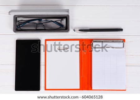 Close up of open diary with a pen, stylish glasses in open case for glasses near mobile phone on wooden white table
