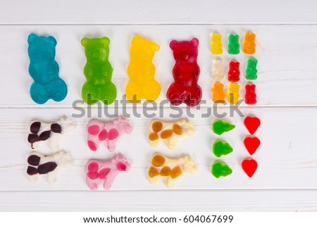Jelly candies in the form of a multicolored big and small gummy bears and cows on wooden white table