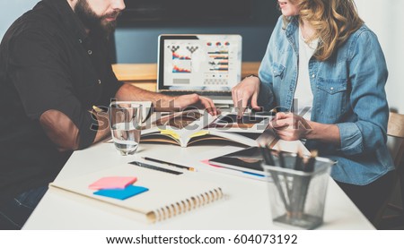 Meet one-on-one. Teamwork. Businesswoman and businessman sitting at table and look in log data. In background laptop with graphs,charts and diagrams on screen. On table is tablet computer, stationery. Royalty-Free Stock Photo #604073192