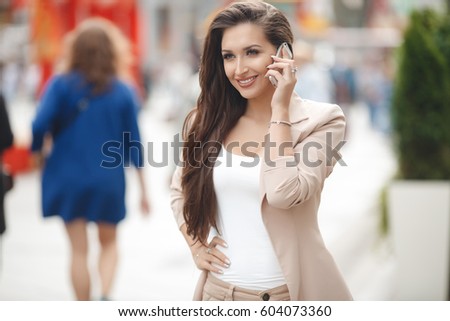 gorgeous beautiful young woman with blonde hair messaging on the smart-phone at the city street background. pretty girl having smart phone  in the street