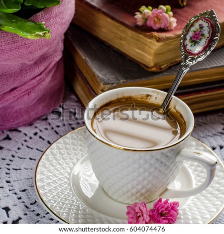 Beautiful still life in vintage style. White Cup of coffee. Beautiful spoon with a picture. Pink fresh flowers. Old books. Selective focus.