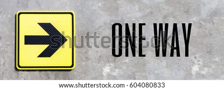 Arrow road sign on a yellow background on a concrete wall with text one way