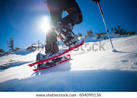 Man in snowshoes with trekking poles is the snow in the mountains. Royalty-Free Stock Photo #604090136