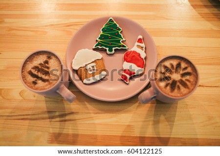 Gingerbreads with Christmas design lie on pink plate between cups with coffee